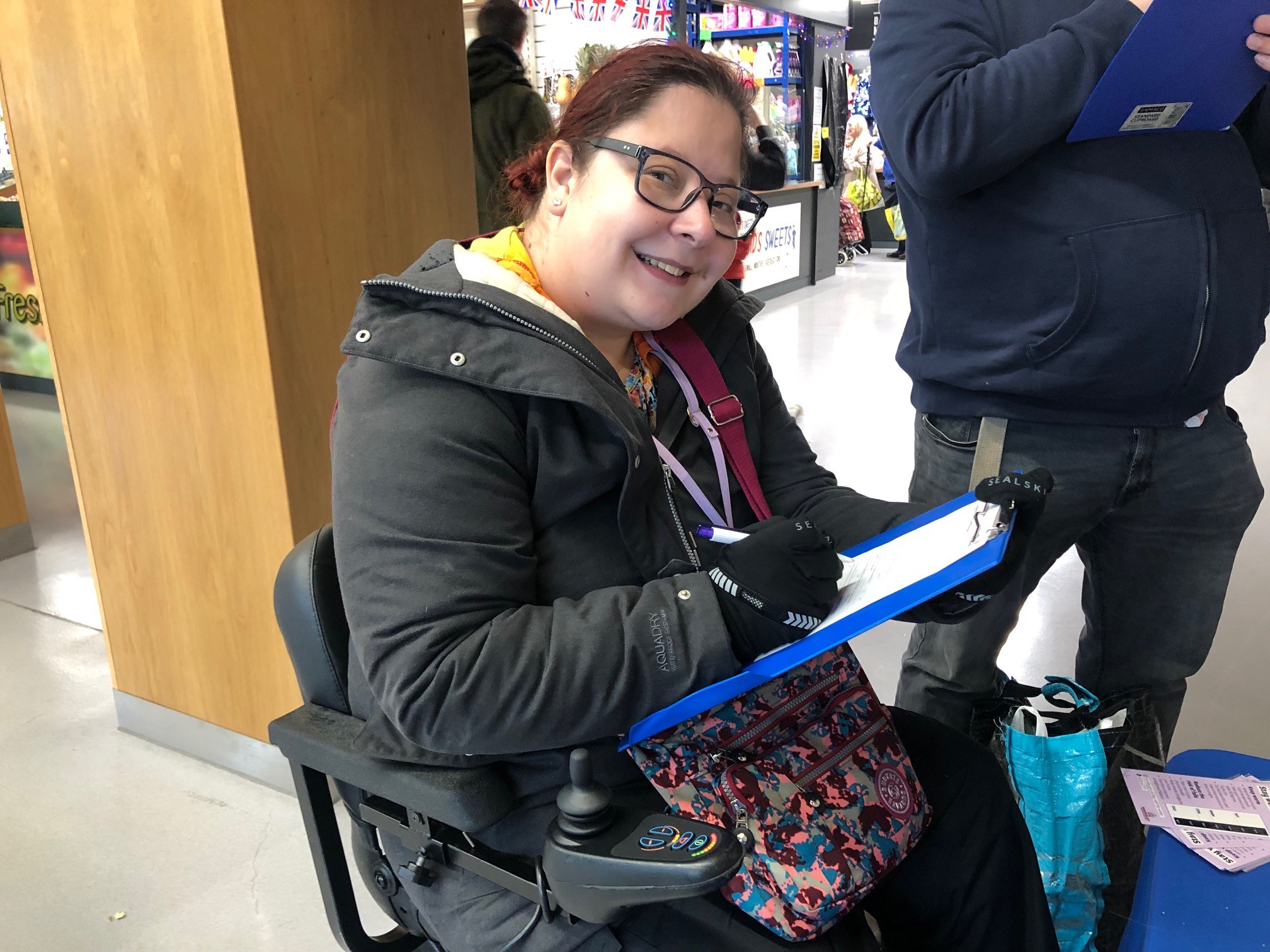 dark haired lady in a black coat sat in a wheelchair completing a survey