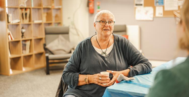 woman_with_white_hair_sitting_at_a_table_whilst_holding_a_cup