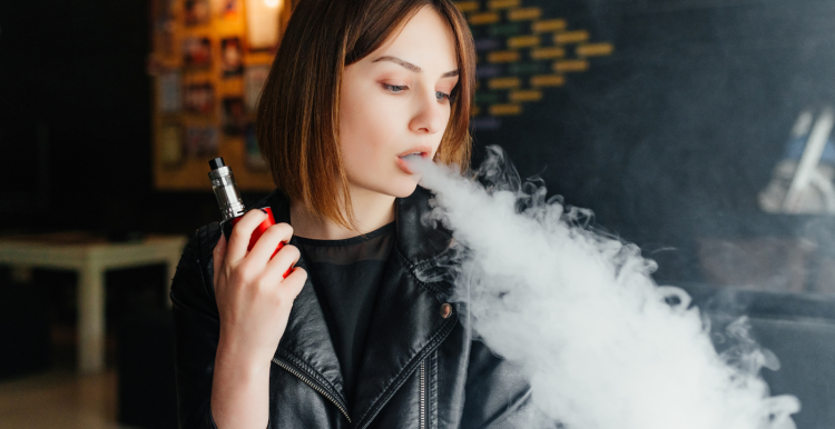 Woman_with_shoulder_length_brown_hair_wearing_a_black_biker_jacket_blowing_out_smoke_from_a_vape_device