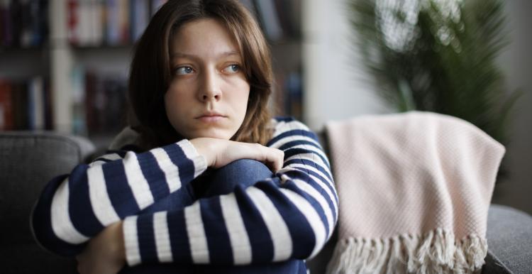 young_waman_wrapping_her_arms_around_her_legs_sitting_on_the_sofa_and_looking_off_to_the_side