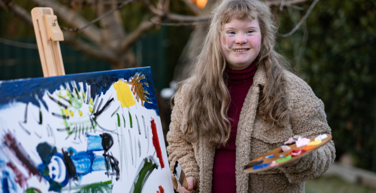 Young_woman_wearing_a_coat_standing_outside_and_painting.She_is_smiling