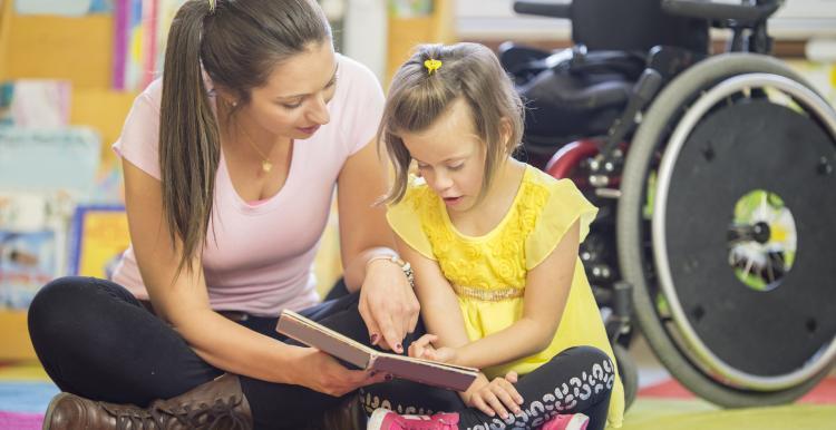 Woman_sitting_on_the_floor_reading_to_a_young_girl_who_has_down_syndrome