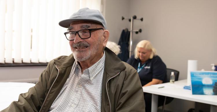 Man_sitting_smiling_wearing_a_flat_cap_and_glasses