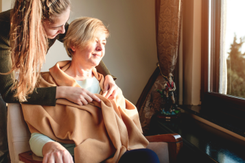 woman_sitting_in_a_chair_being_covered_with_a_blanket_by_a_younger_woman