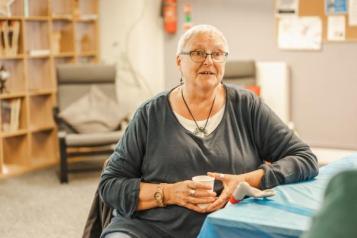 woman_with_white_hair_sitting_at_a_table_whilst_holding_a_cup