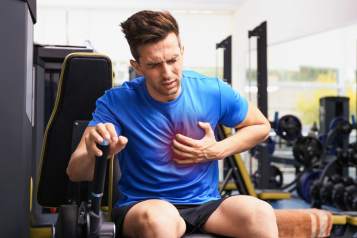 young_man_sitting_in_the_gym_clutching_his_chest