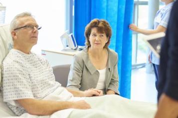 Man_sitting_in_a_hopsital_bed_with_a_woman_visitor_at_his_side_listening_to_a_doctor