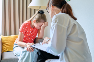 young_girl_sitting_with_her_head_in_her_hand_with_a_female_doctor_talking_to_her