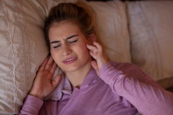 woman_holding_her_jaw_in_pain_and_lying_on_a_bed