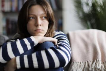 young_waman_wrapping_her_arms_around_her_legs_sitting_on_the_sofa_and_looking_off_to_the_side