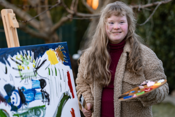 Young_woman_wearing_a_coat_standing_outside_and_painting.She_is_smiling