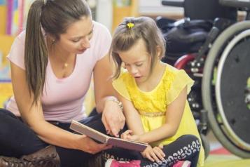 Woman_sitting_on_the_floor_reading_to_a_young_girl_who_has_down_syndrome