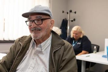 Man_sitting_smiling_wearing_a_flat_cap_and_glasses