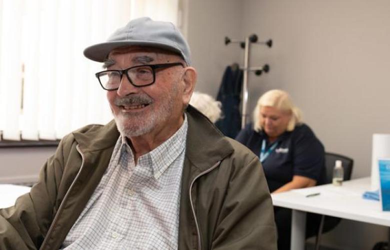 Man_sitting_smiling_wearing_a_flat_cap_and_glasses